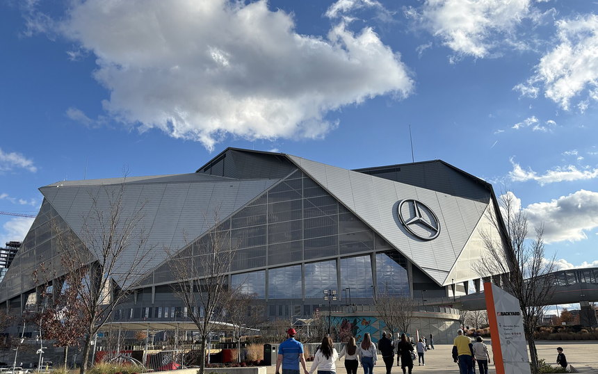 The folding roof and glass facade of Mercedes-Benz Stadium, people crossing the plaza in front of it