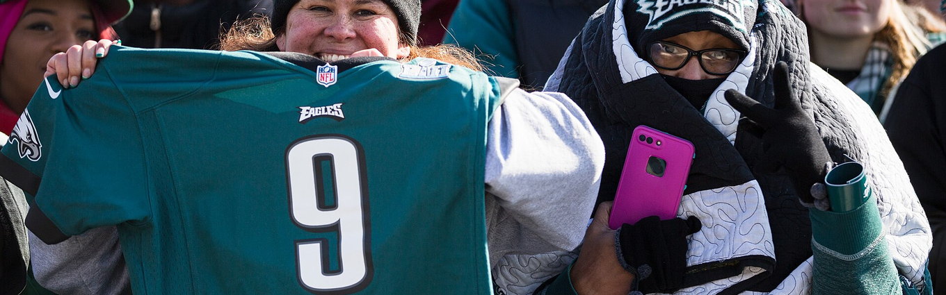 Fans in Eagles jerseys and winter hats pressed against a barrier along a parade route