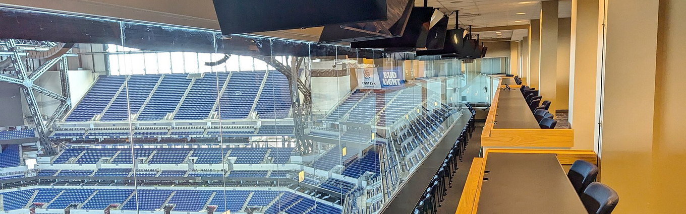 A long counter of seats and monitors in a stadium press box looking down on the field