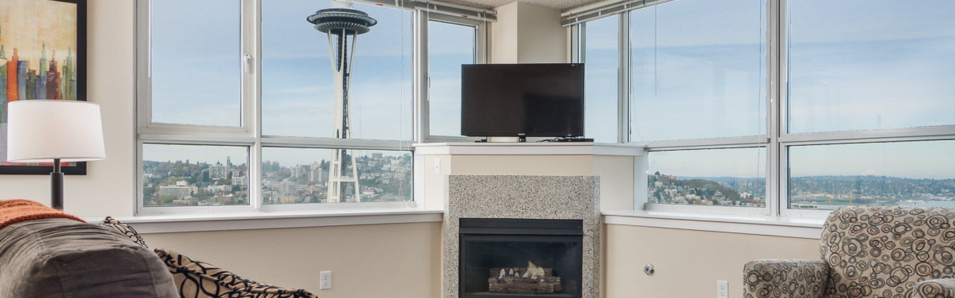 A furnished living room with floor-to-ceiling windows looking out over Seattle, the Space Needle visible outside