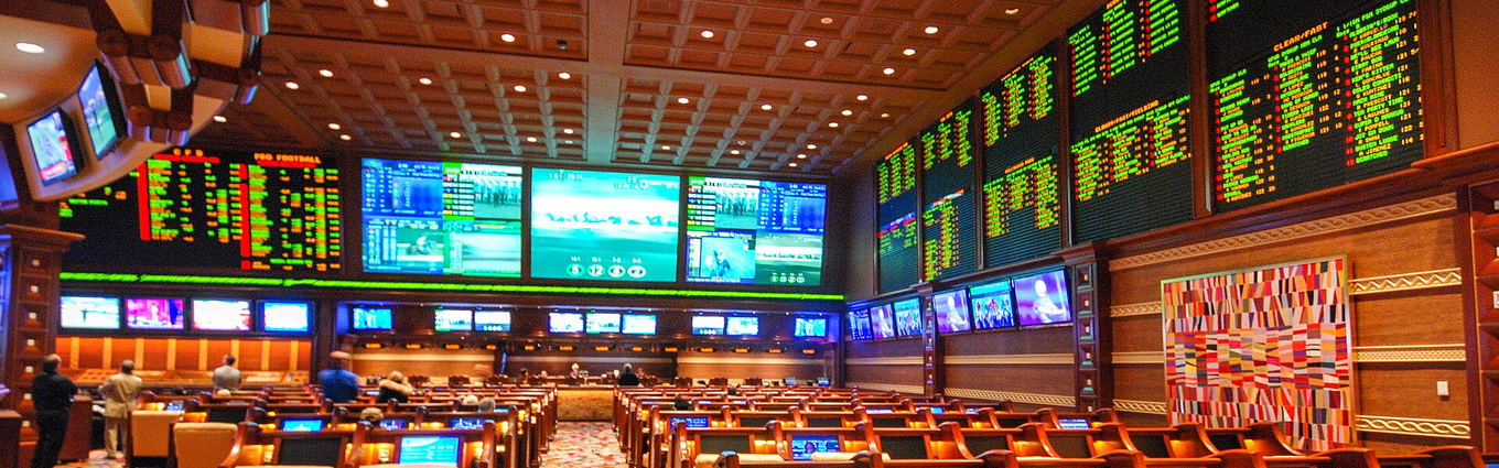 A casino sportsbook, walls of odds boards and screens above rows of armchairs