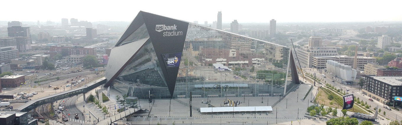 The angled glass front of U.S. Bank Stadium seen from the air over downtown Minneapolis